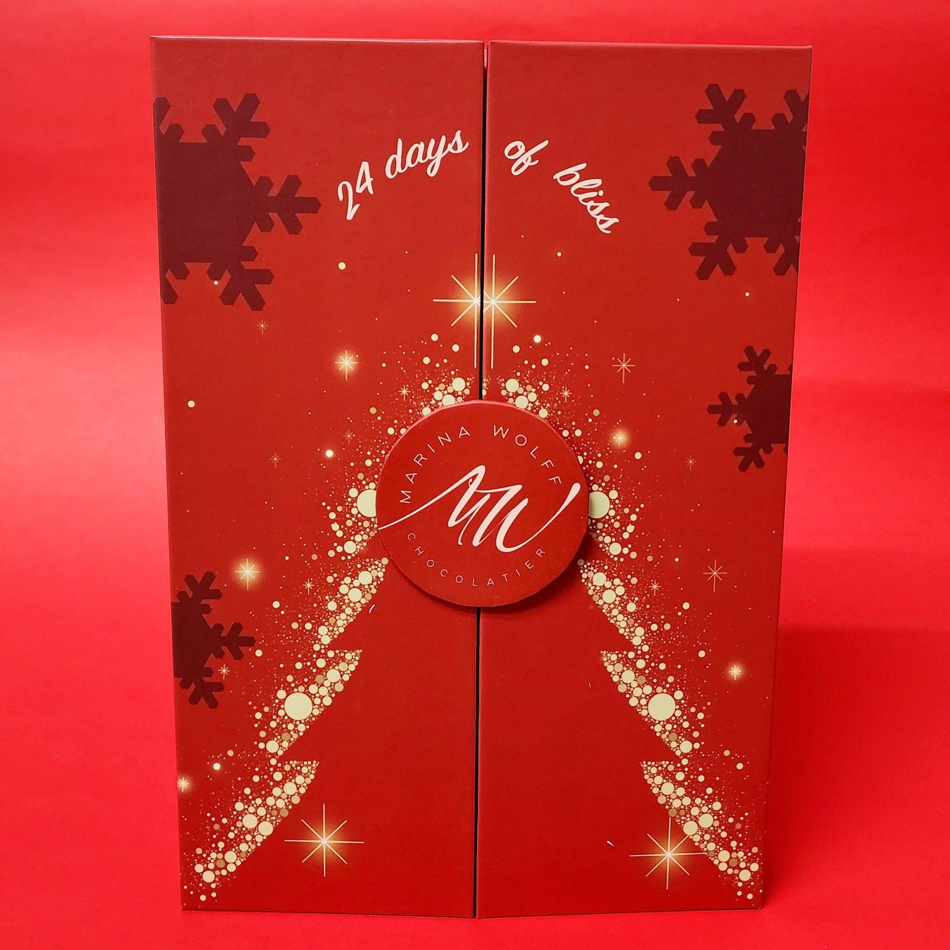 A red rectangular box with a silhouette of a tree surrounded by snowflakes and stars written ' 24 days of bliss' on top of it on a red background.