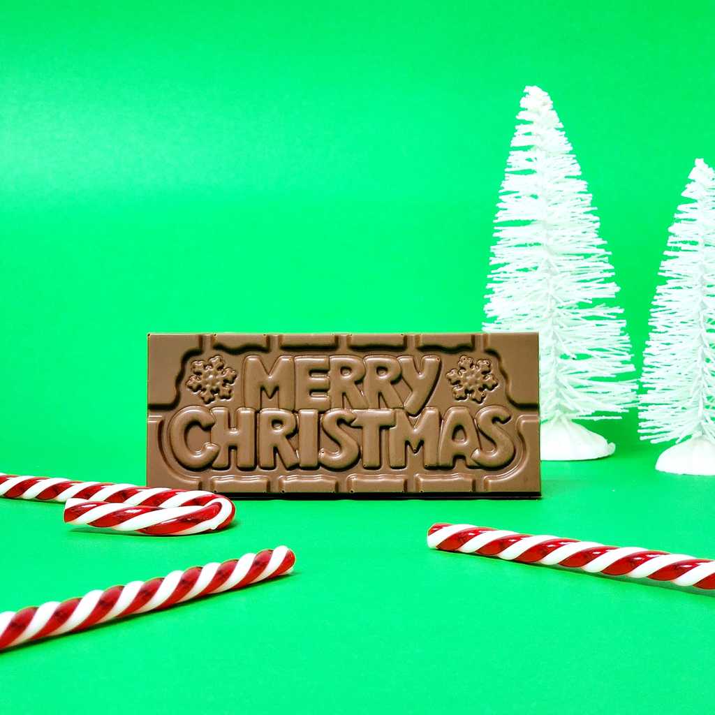 Milk chocolate bar with Merry Christmas written on it with white trees and candy cane on a green background